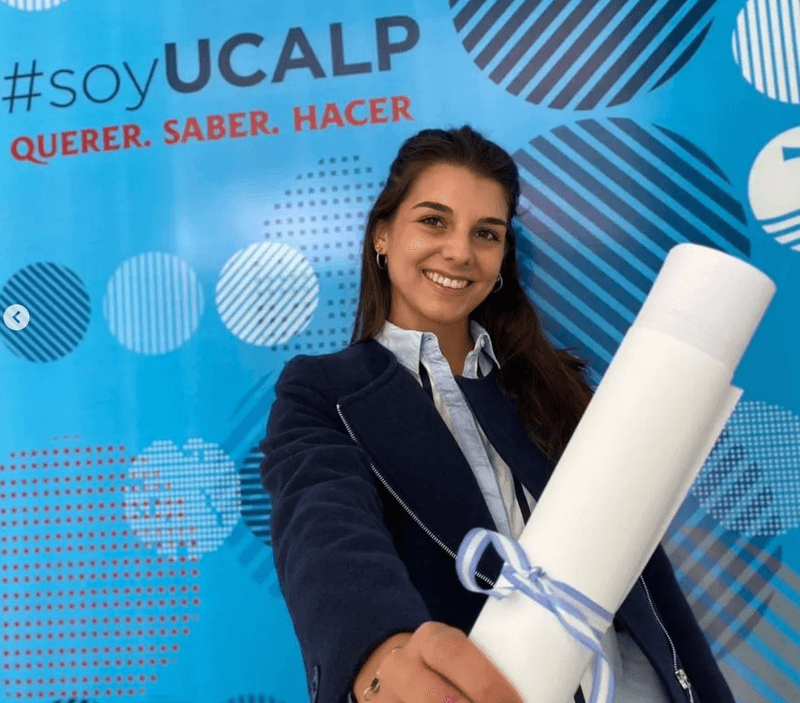 Valentina sosteniendo un diploma frente al fondo de UCALP